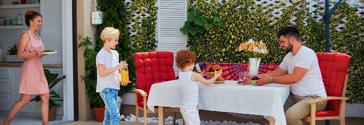 Eine Familie isst auf der Terrasse unter einem großen Sonnenschirm.